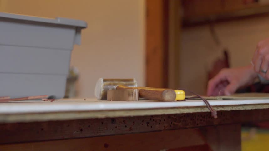 A man picks up leather from a worktable with tools on it