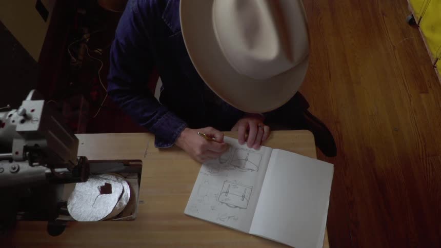 A man sketches a pattern at a sewing desk