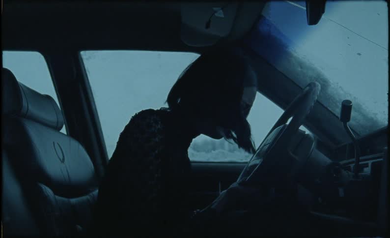 The woman leans forward crying in the car