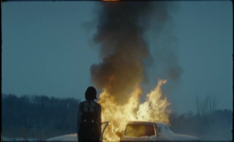 The woman watches the car burn in the snow