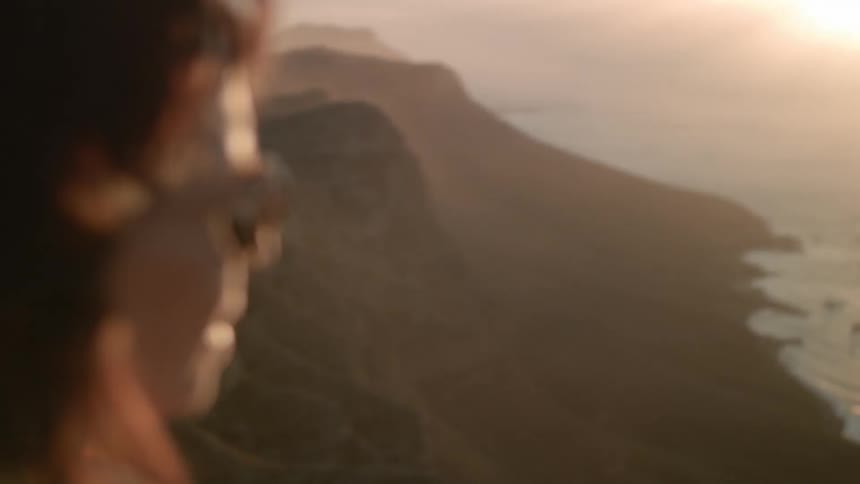 A woman stand above looking out at the ocean from a cliff line