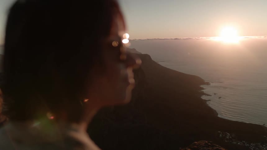 A woman takes a photograph of the ocean at sunset