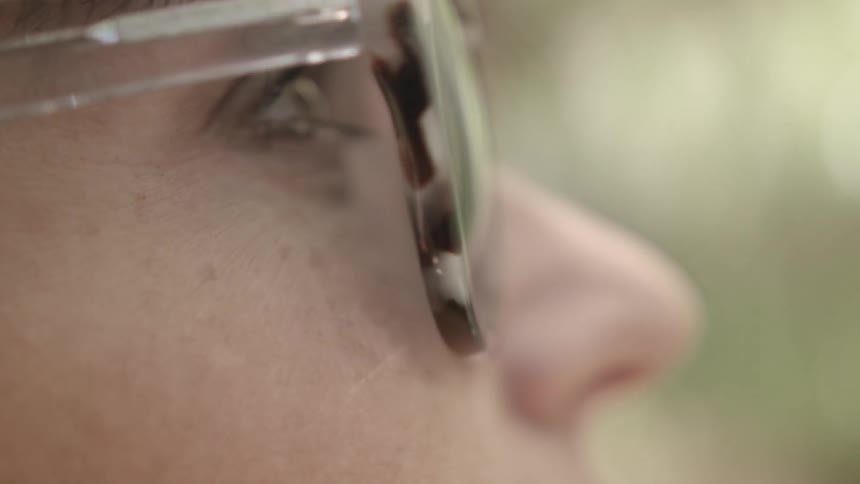 A woman wears sunglasses and looks towards the sky