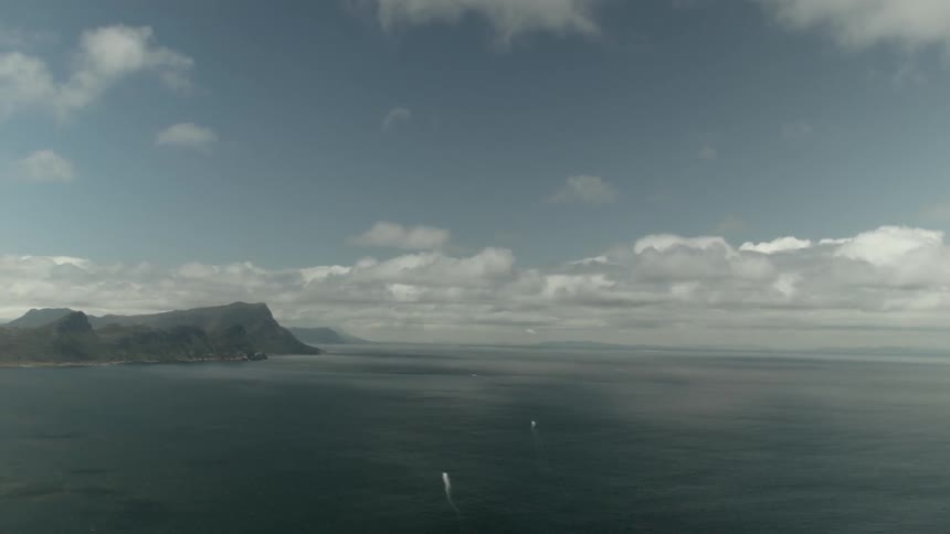 Boats travelling on a body of water with cliffs and clouds in the background