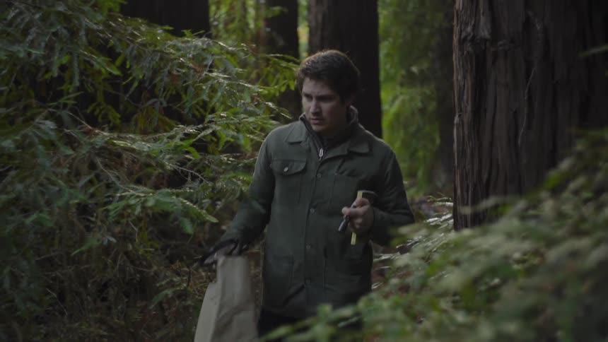 A man with a bag and flashlight walks through the woods