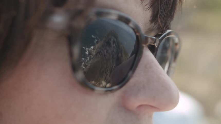 Brunette person wearing sunglasses that reflect mountain scenery