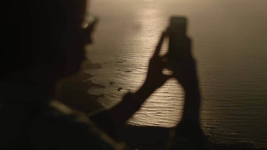 A woman uses an iphone to take a picture near the beach