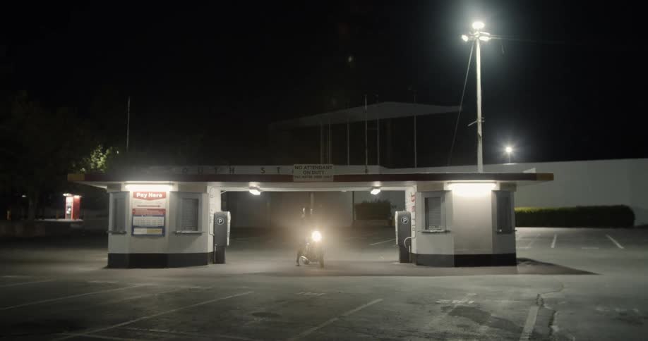 A motorcyclist is stopped in a parking lot at night