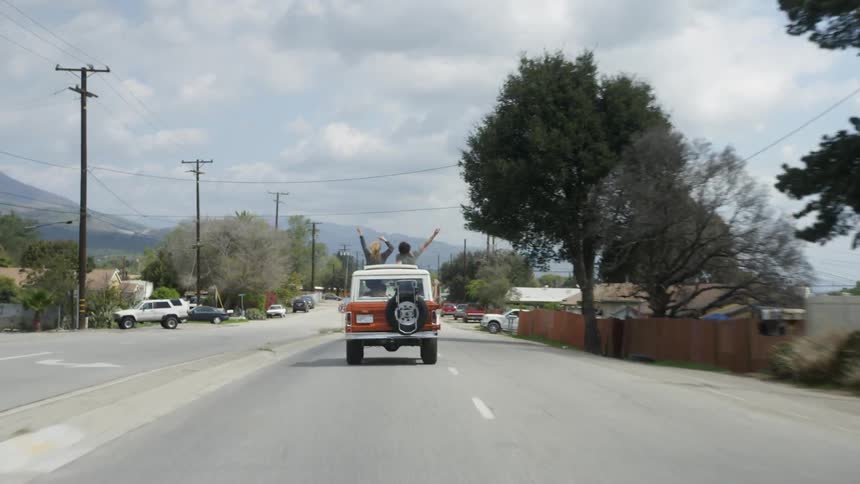 Two people stand through an open car roof while riding down a street