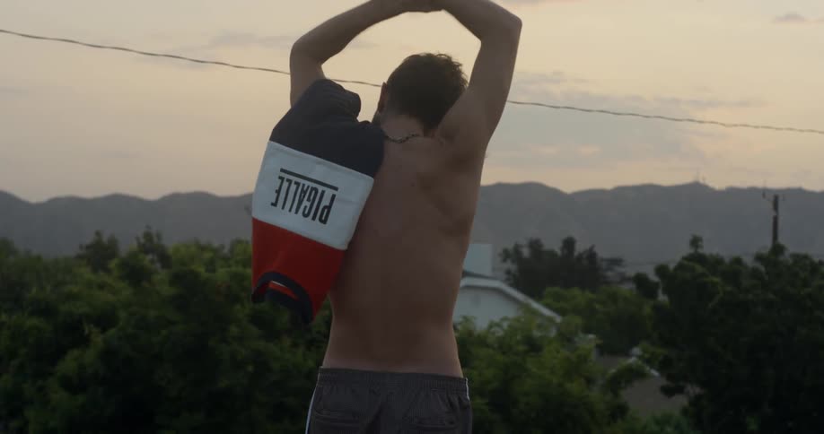 Shirtless man stretches at sunset