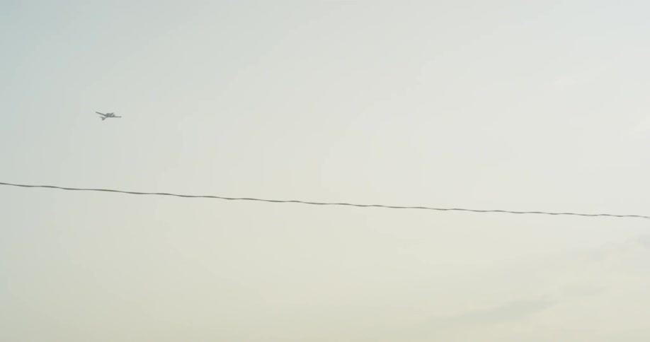 The plane flies high in the cloudy sky