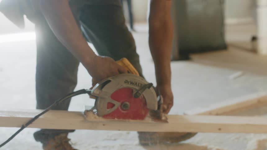 A construction worker cuts wood with a saw