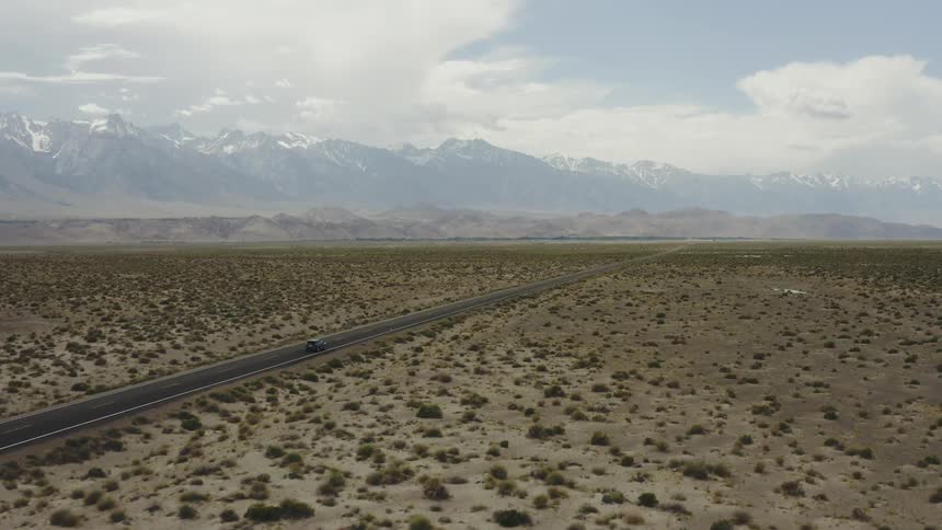 Camera follows lone car traveling down desolate desert highway