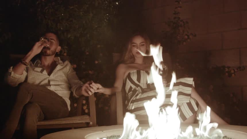 A couple holds hands and drinks wine while sitting by a fire ring