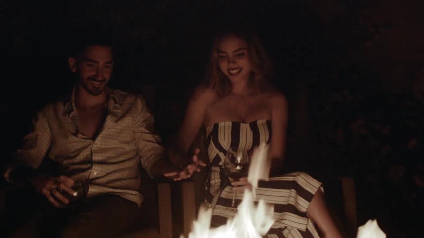 A man and woman talk by the fire at night