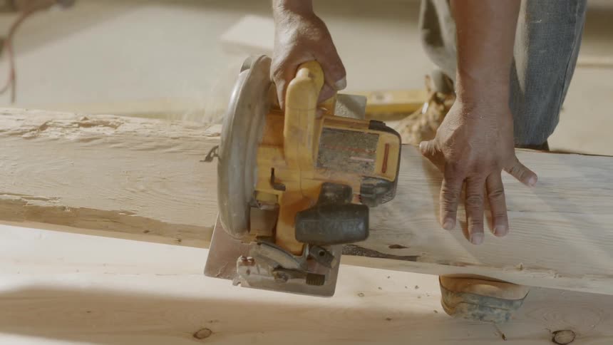 A construction worker cuts wood with a saw
