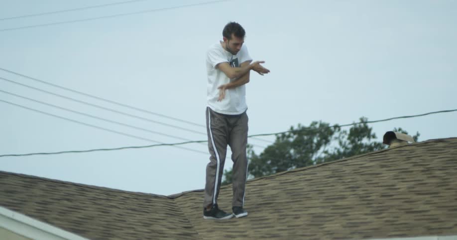 A man dances and stretches on the roof of a house