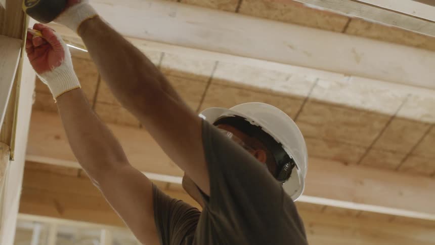 A man is marking a wood board in a construction project in daylight