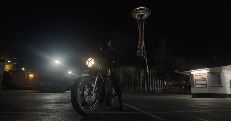A motorcyclist is stopped in a parking lot at night