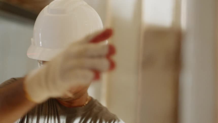 Man wearing a hardhat and safety goggles adjusts some wood