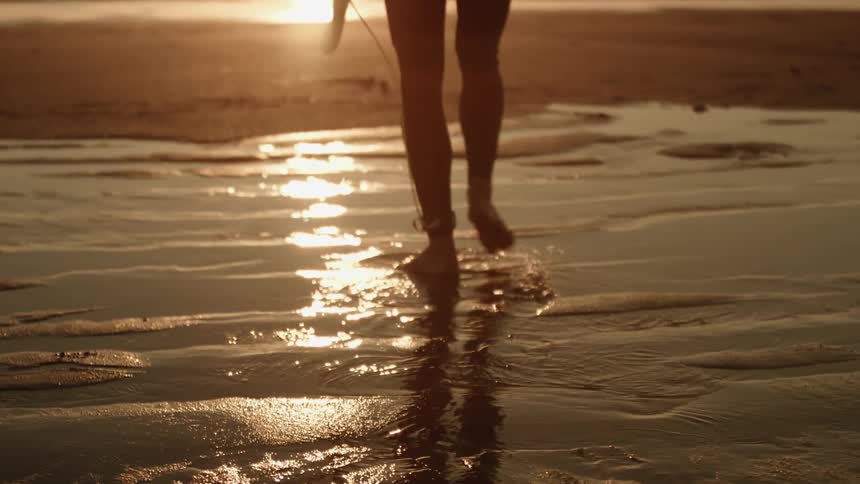 Person carries a surfboard walking on wet sand