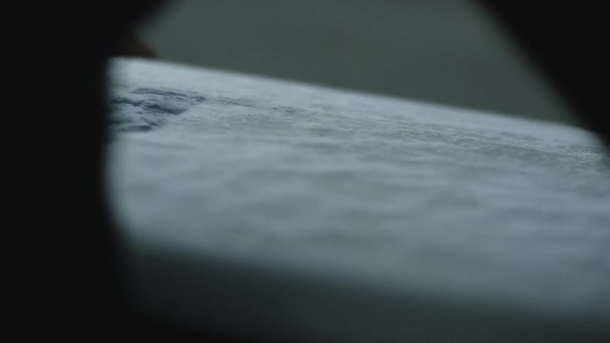 A woman is waxing a surfboard inside in daylight