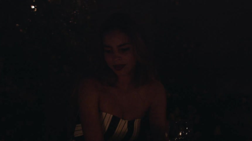 A woman sits outside of a fire with a wine glass