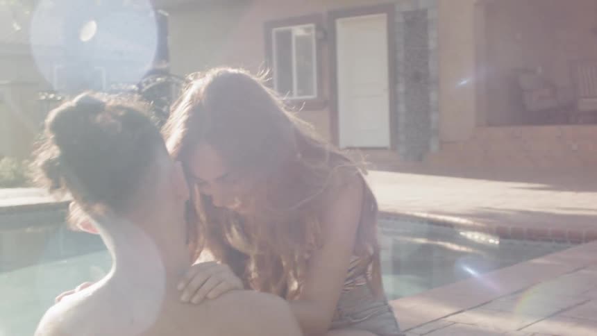 A man and woman laugh and flirt poolside on a sunny day