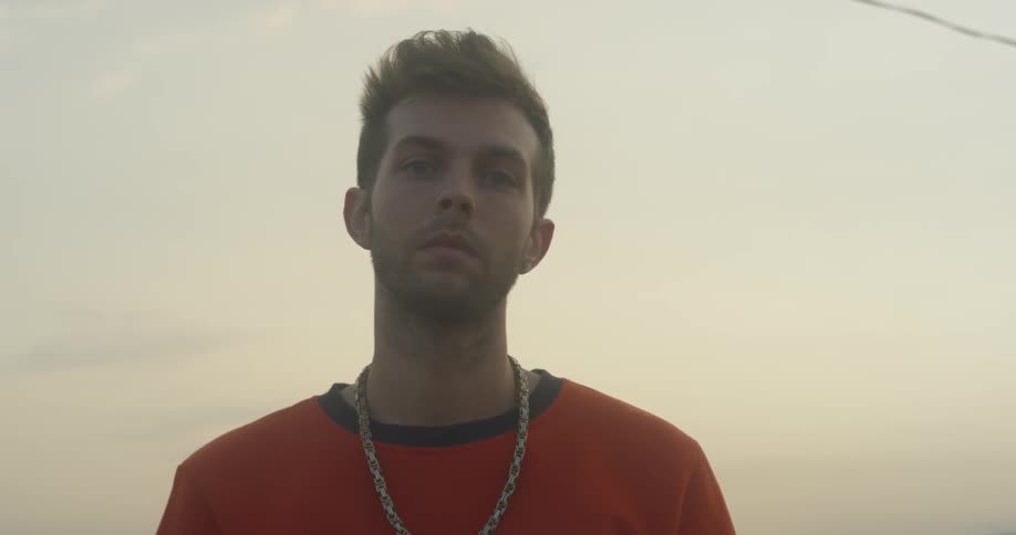 A man wearing a chain stands outside