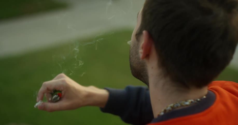 A man holds his lighter in his hand as he smokes a cigarette outside
