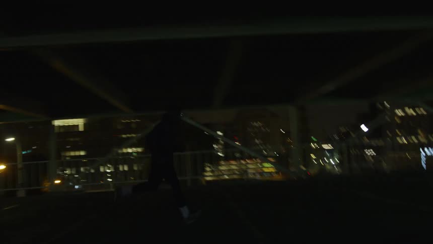 A man jogs through a parking level with city light shining