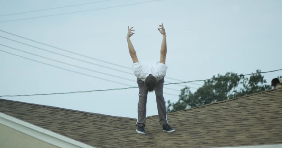 A man is stretching and bending as he stands outside on a roof in daylight
