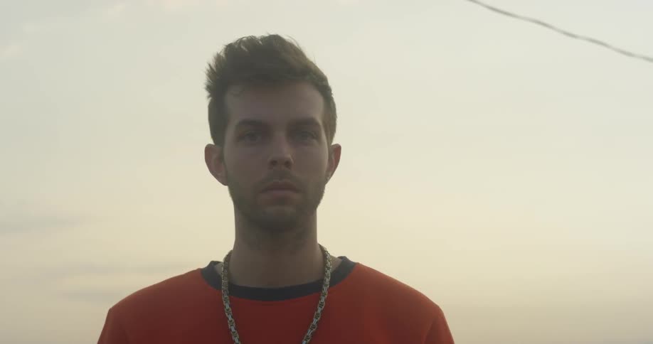 A man wearing a chain necklace looks around outside