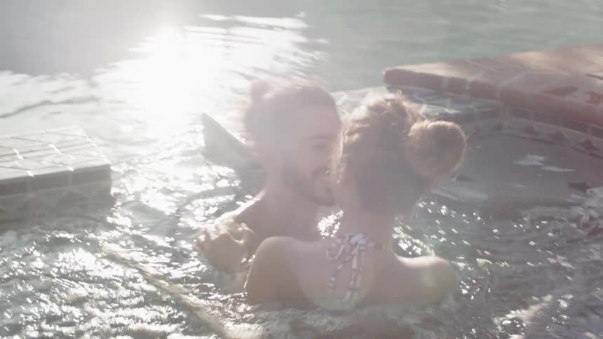 A man and woman flirt in an outdoor hot tub
