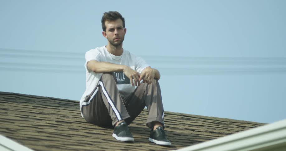 A man is looking pensive as he sits on a house on a sunny day