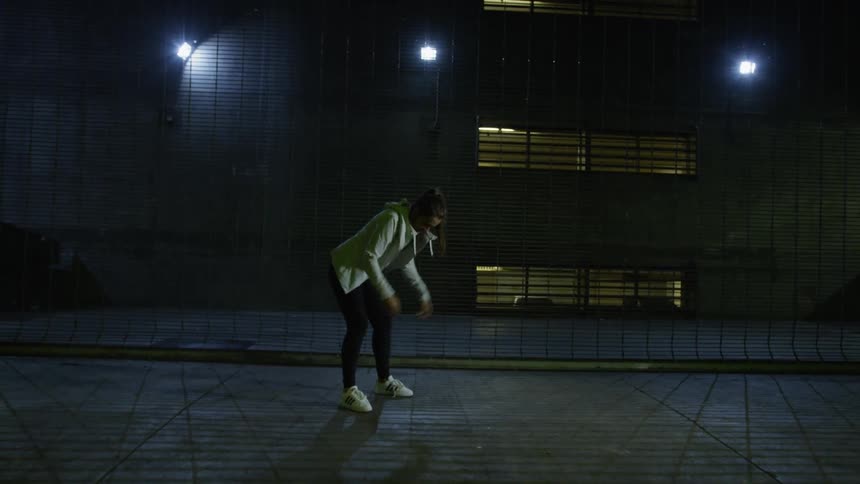 A woman running at night pauses to catch her breath and then runs again