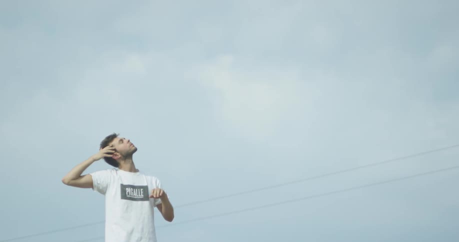 A man is moving his arms around his face in an expressive motion outside on a cloudy day