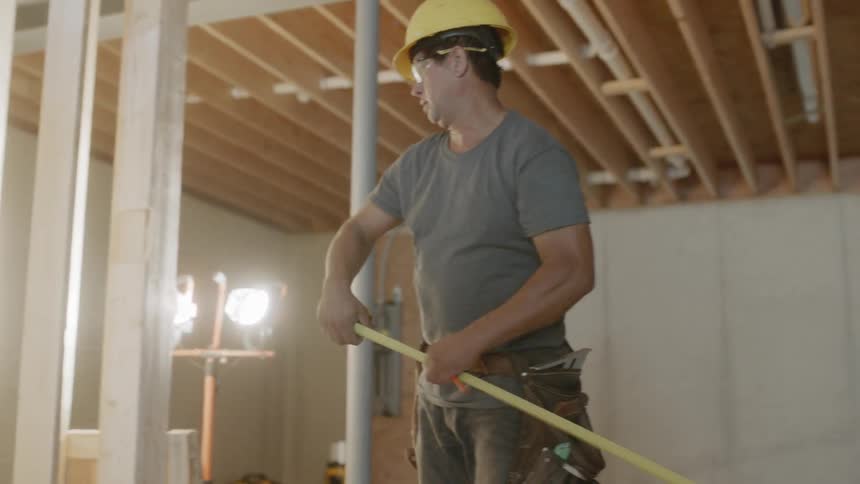 Man wearing a hard hat uses a measuring tape
