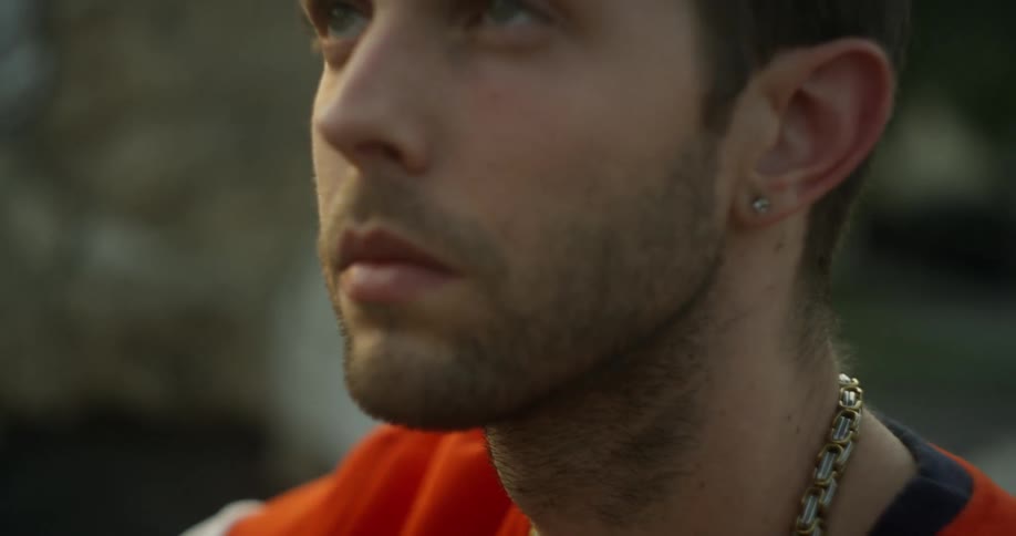 Man wearing gold chain is sitting outside and staring upwards