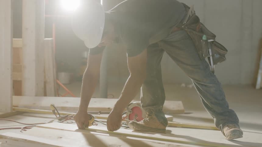 A worker is measuring a board inside a construction project in daylight