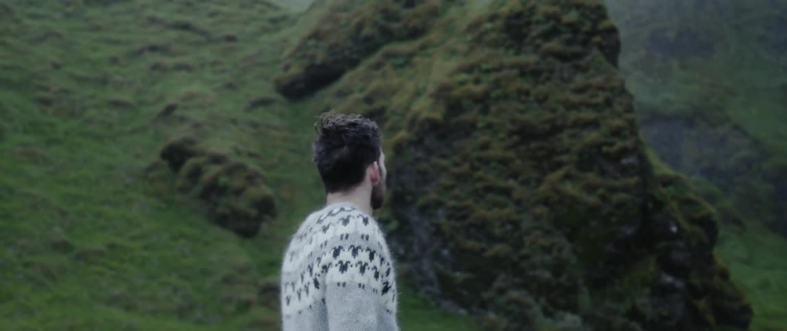 A man wearing a sweater stands next to a river