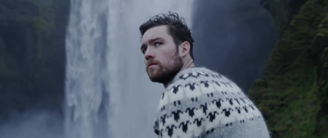 A man stands near a waterfall in the wilderness