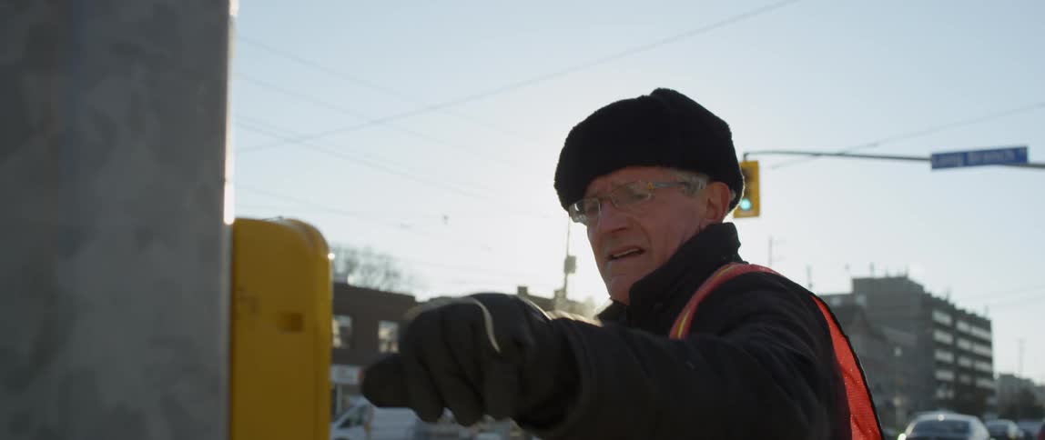 Elderly man repeatedly pushes a button on a machine outside in the city