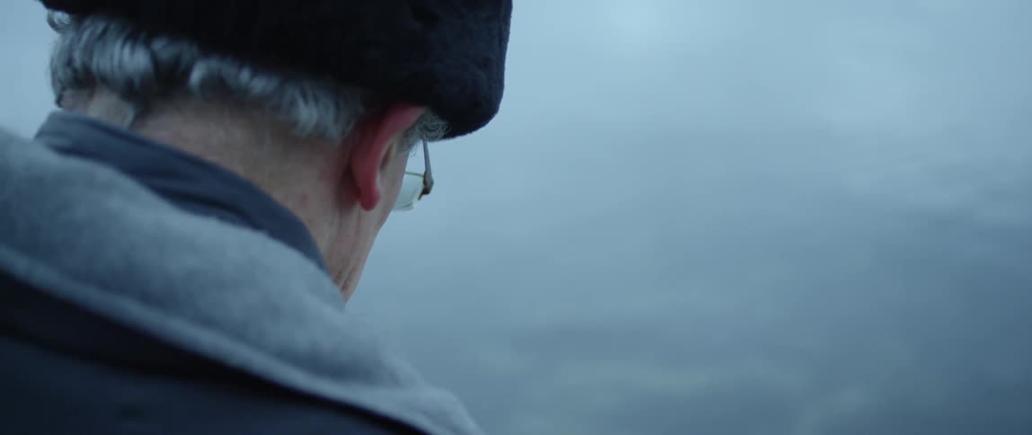 A man sits next to a lake on a cold day