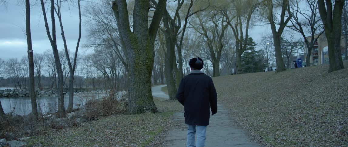 A man walks on a path near a pond on a cloudy day