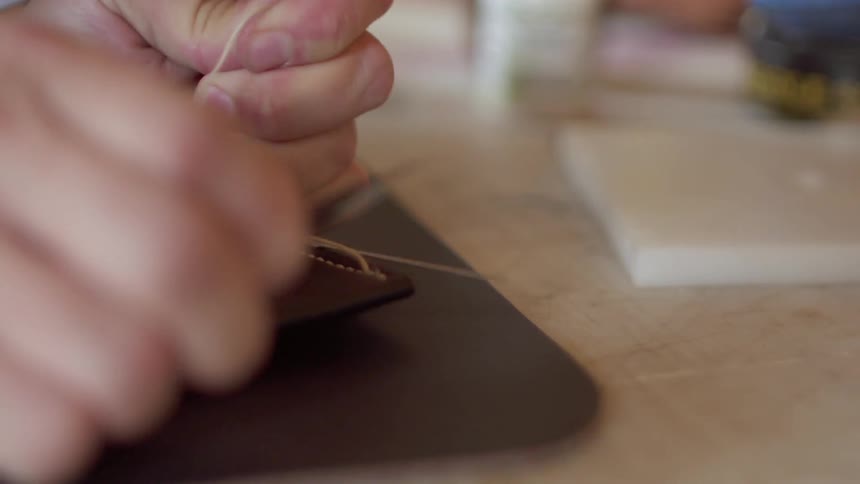 A person trims the thread ends from a stitched piece of leather