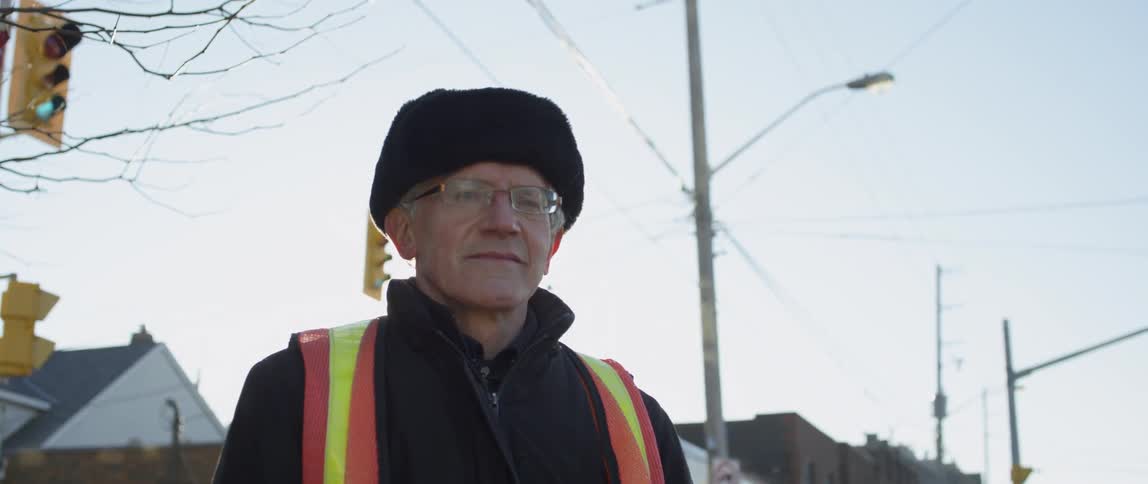 A traffic guard wears an orange vest outside