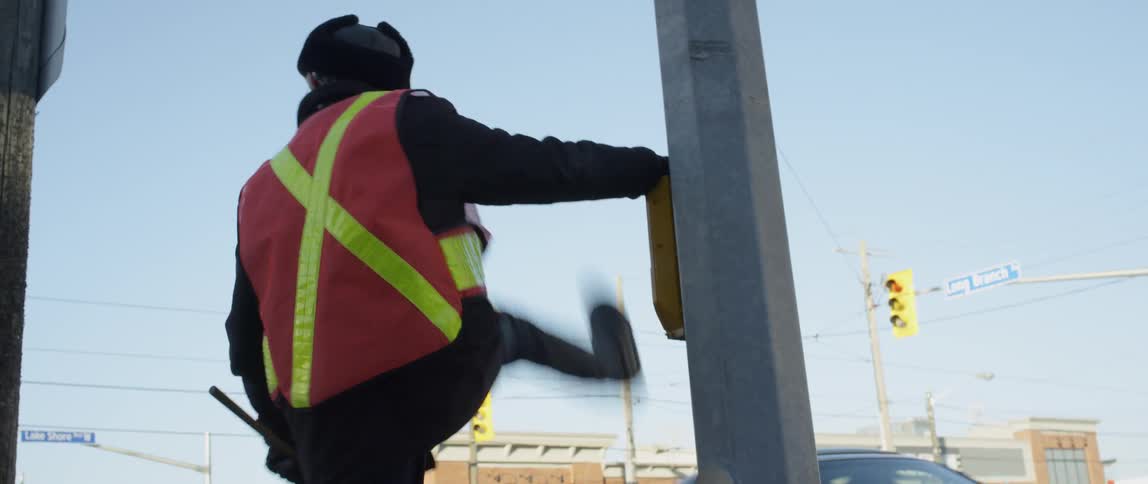 A crossing guard kicks his leg out on the corner on a sunny day