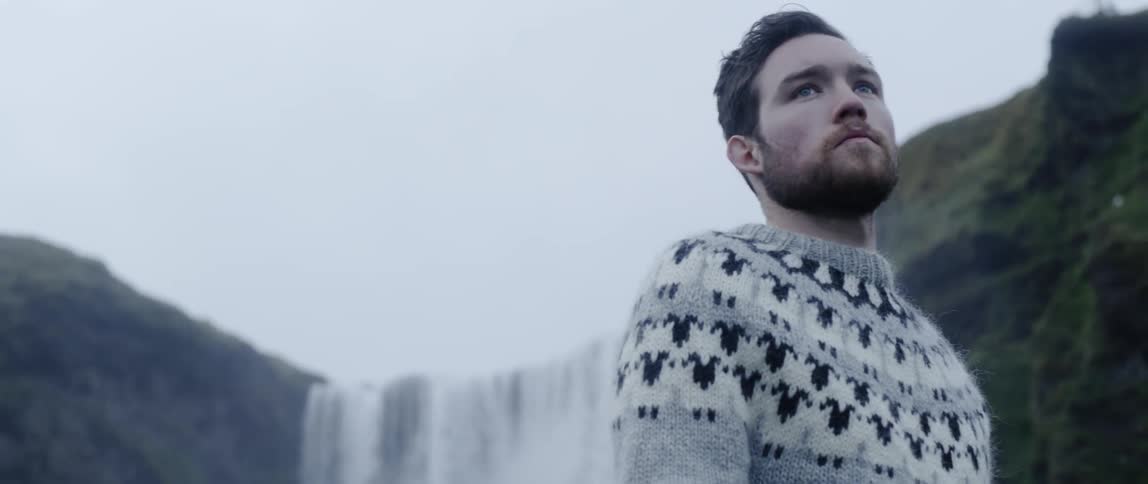 Man blows into his hands as he stands near a waterfall