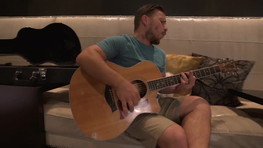 Man sings as he plays the guitar while sitting on a sofa